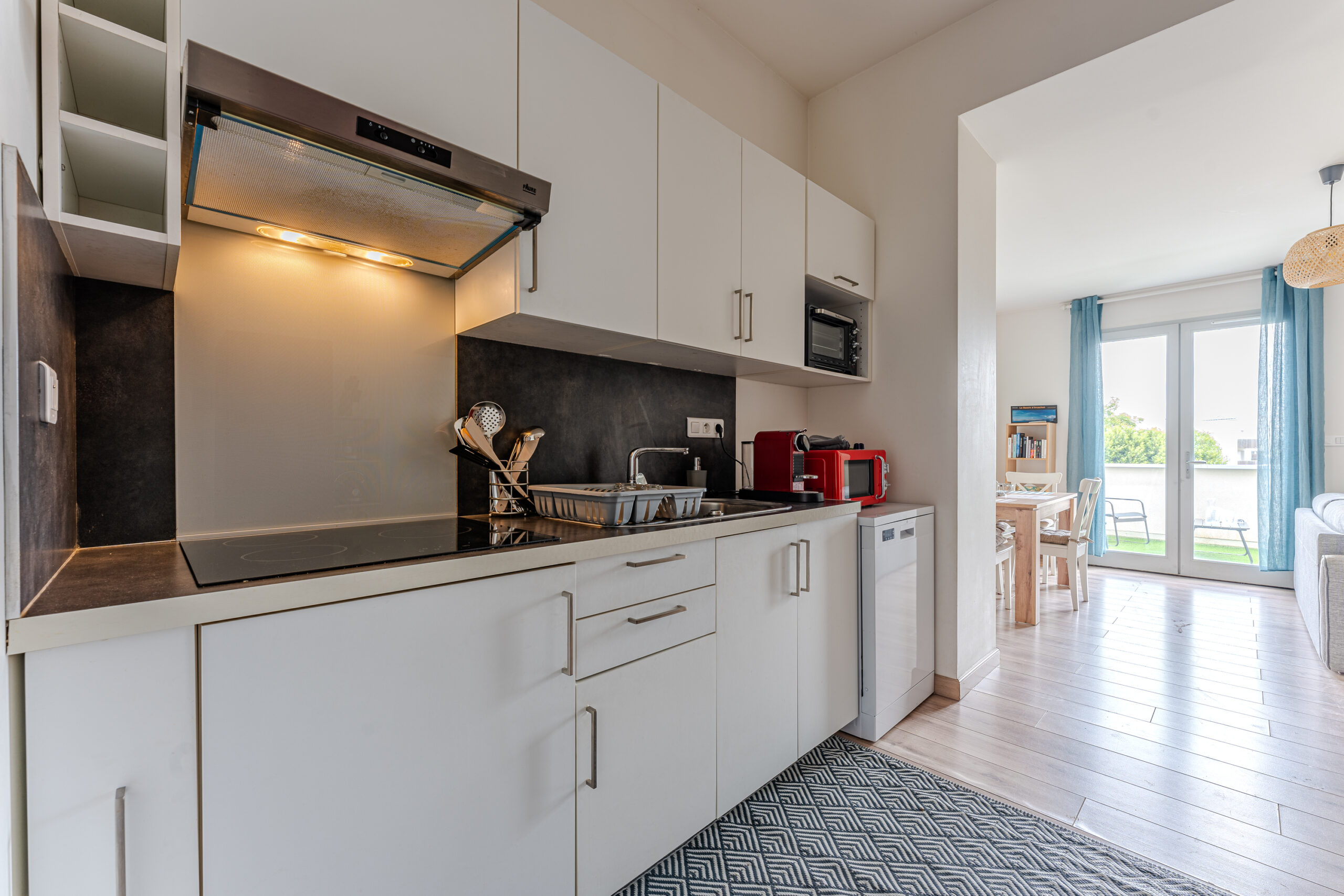 Photo de la cuisine bien équipée de l'appartement, mettant en avant des appareils modernes tels qu'une cafetière Nespresso, un micro-ondes, et un mini-four. Les plans de travail propres et spacieux, ainsi que les placards bien agencés, offrent un espace fonctionnel et élégant pour préparer des repas. L'ambiance est rehaussée par une décoration minimaliste et une lumière naturelle, créant un environnement accueillant pour cuisiner et se détendre.