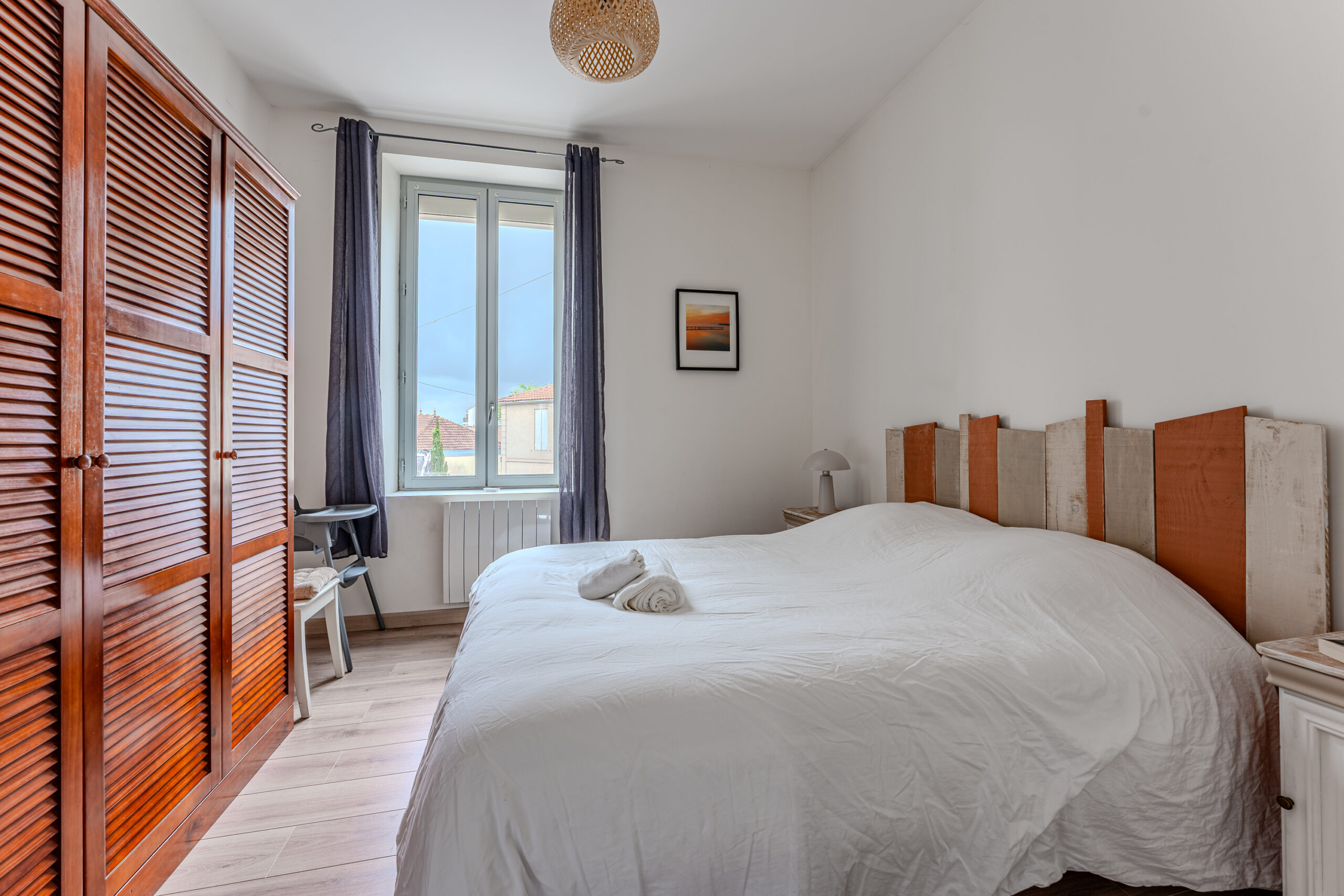 Intérieur de la chambre à coucher montrant un grand lit avec literie de qualité, un grand placard et un coin dressing pour le rangement, et une décoration minimaliste et élégante. La chambre est baignée de lumière grâce à une fenêtre qui offre également une vue apaisante sur les environs, offrant un espace de repos accueillant et paisible.